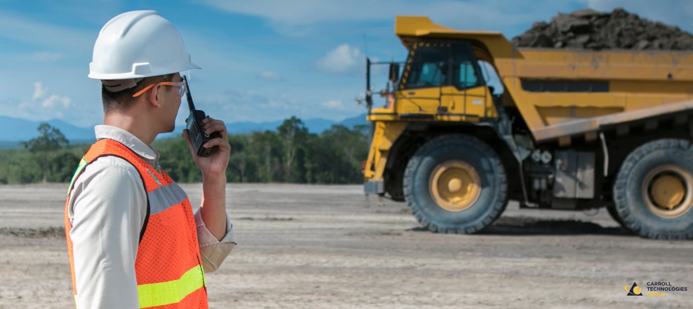 Mine safety representative wearing PPE and talking on mine radio with mine truck in distance